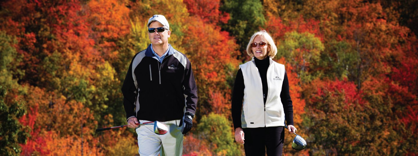 Couple holding golf clubs with fall foliage behind them