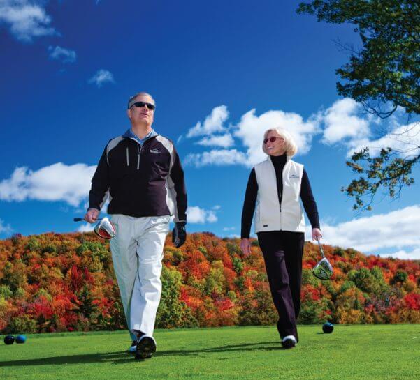 Couple holding golf clubs with fall foliage behind them