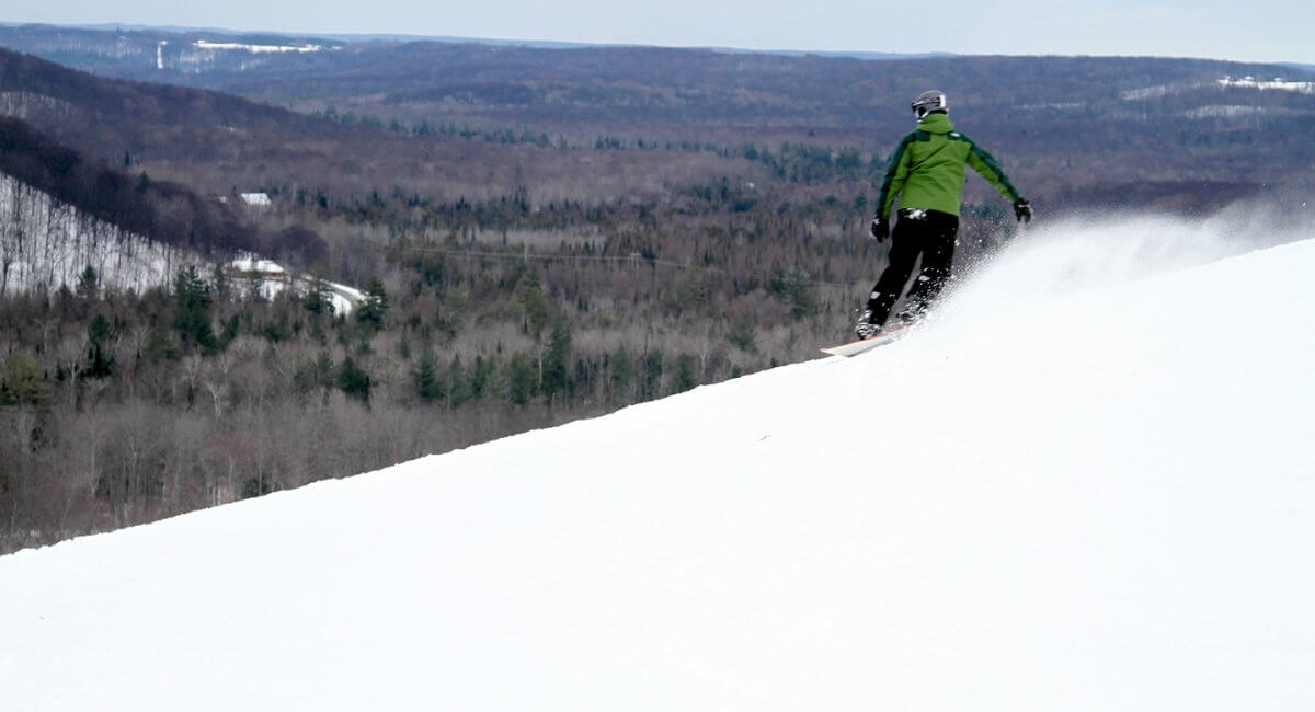 Snowboarder in green jacket on top of Schuss Mountain