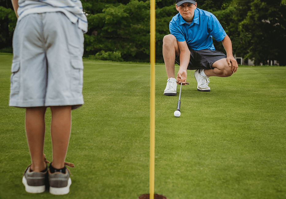 Junior lining up putt. Another junior tending the flag for him.