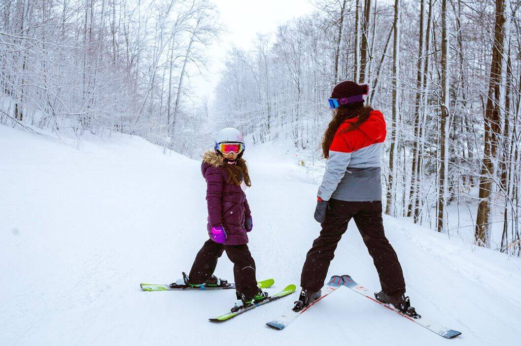 Mother and daughter on skis looking backwards at camera