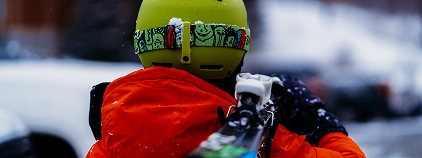 Photo of skier from behind, carrying skis on his shoulder