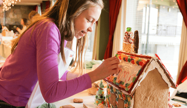 girl in pink decorating roof of a gingerbread house