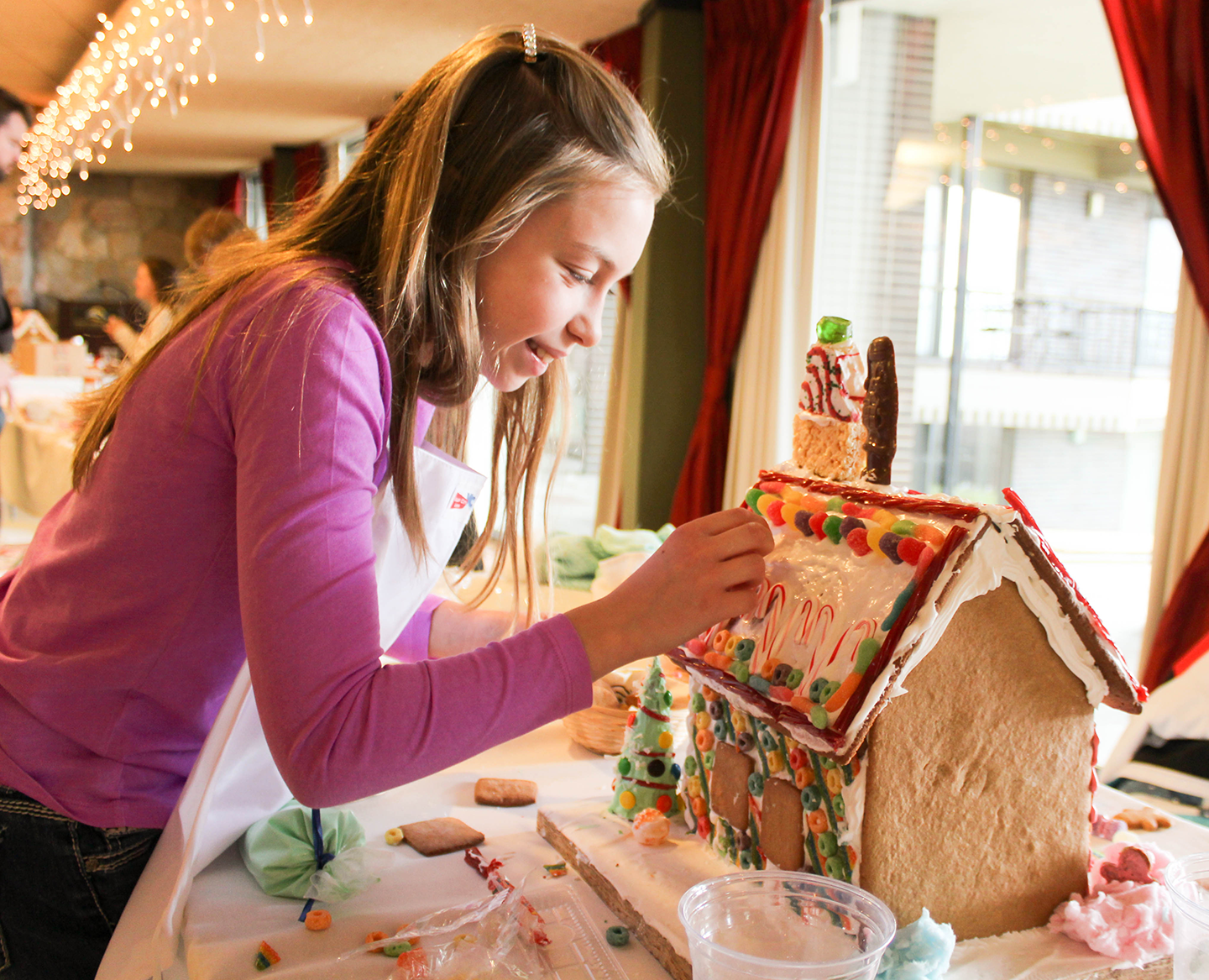 girl in pink decorating roof of a gingerbread house