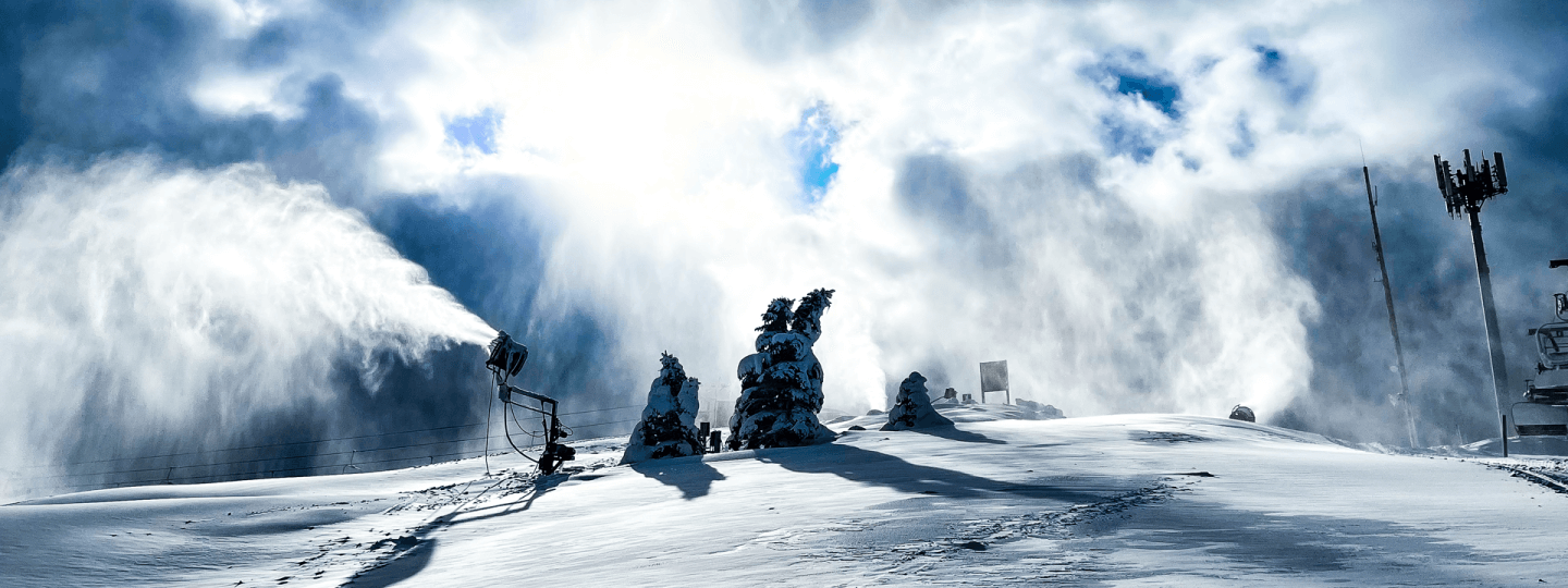 Top of Schuss Mountain covered in snow with snowguns blowing and blue skies