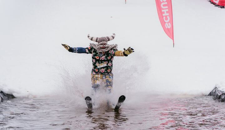 Man dressed in Hawaiian Print Clothing with Viking hat and beard skiing across the slush cup pond