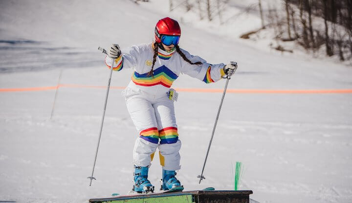 Skier in Retro Rainbow Snowsuit hitting a box rail in the Low Rider Terrain Park
