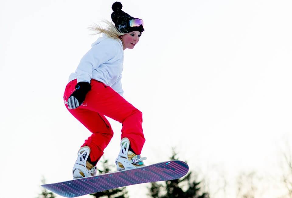 Female snowboarder taking a jump in the Purple Daze Terrain Park