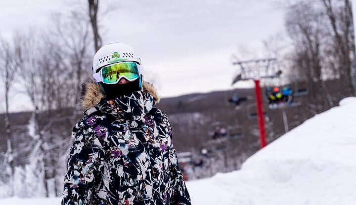 Snowboarder with Goggles Posing in front of the Red Chairlift in a Black, White and Purple Coat