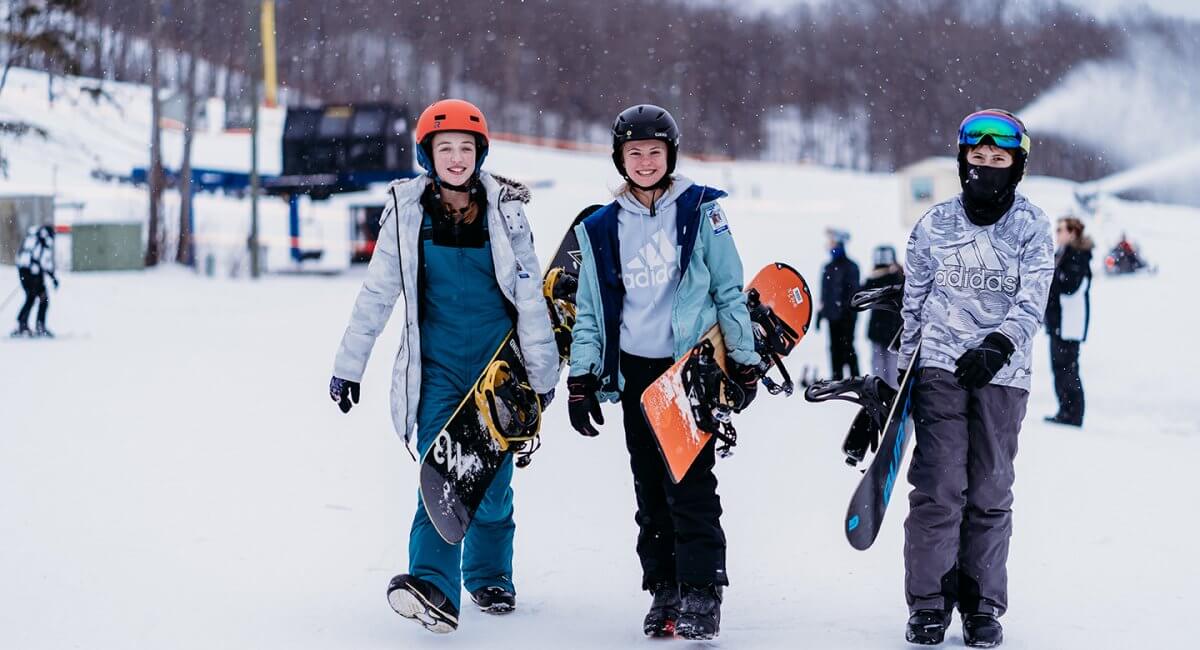 Group of Three Youth Snowboarders carrying their snowboards near the yellow chairlift