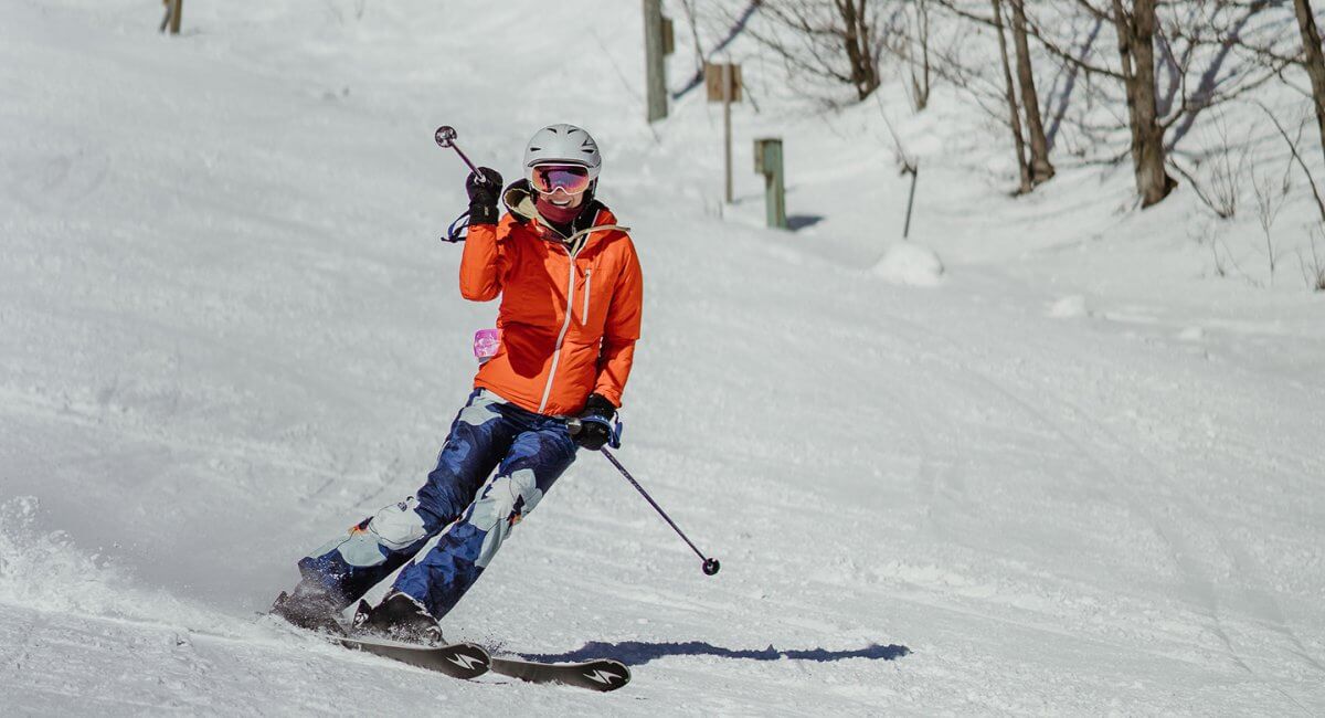 Skier in Orange Jacket and Blue Camo Pants Skiing Down the Hill