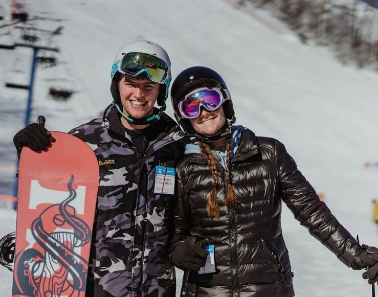 Male Snowboarder and Female Skier pose in front of the Blue Chairlift at Schuss Mountain