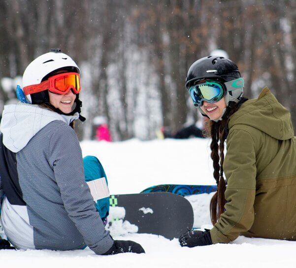 Two snowboarders strapping in turned around looking at the camera