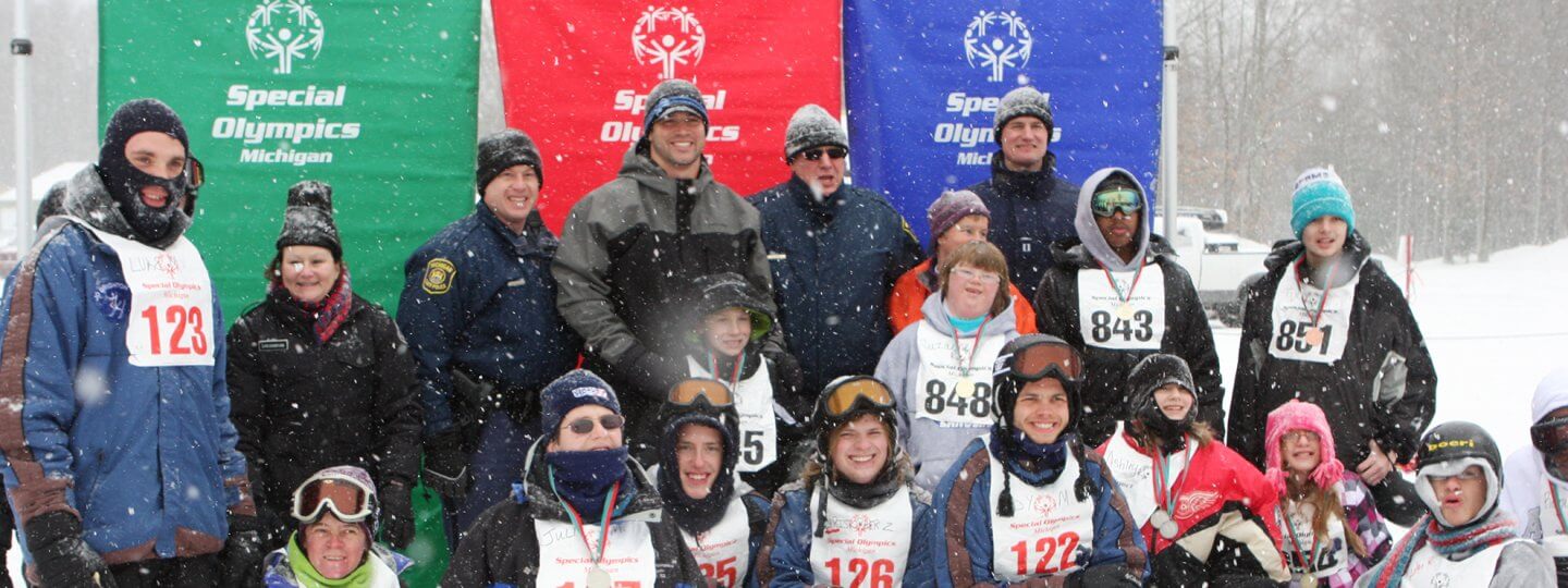 Participants of the Special Olympics Winter Games pose in front of Special Olympics banners displaying their medals.