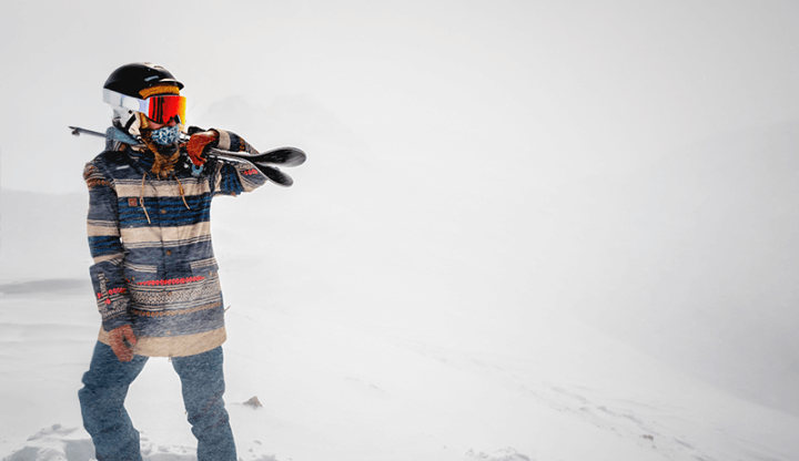 Skier holding skis wearing jeans, goggles and a helmet