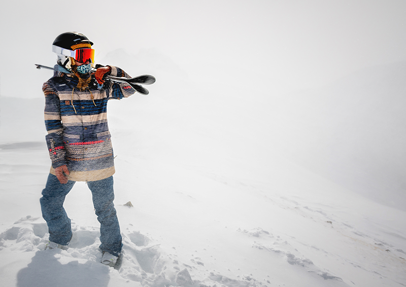 Skier holding skis wearing jeans, goggles and a helmet